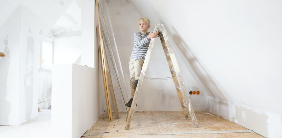 Boy standing on ladder in attic to be renovated