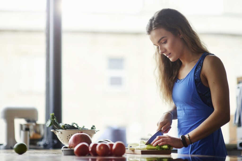 Young woman at kitchen table slicing vegetables