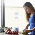 Young woman at kitchen table slicing vegetables