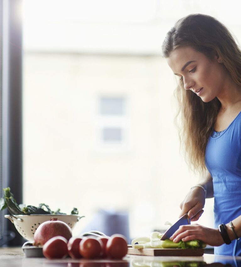 Young woman at kitchen table slicing vegetables
